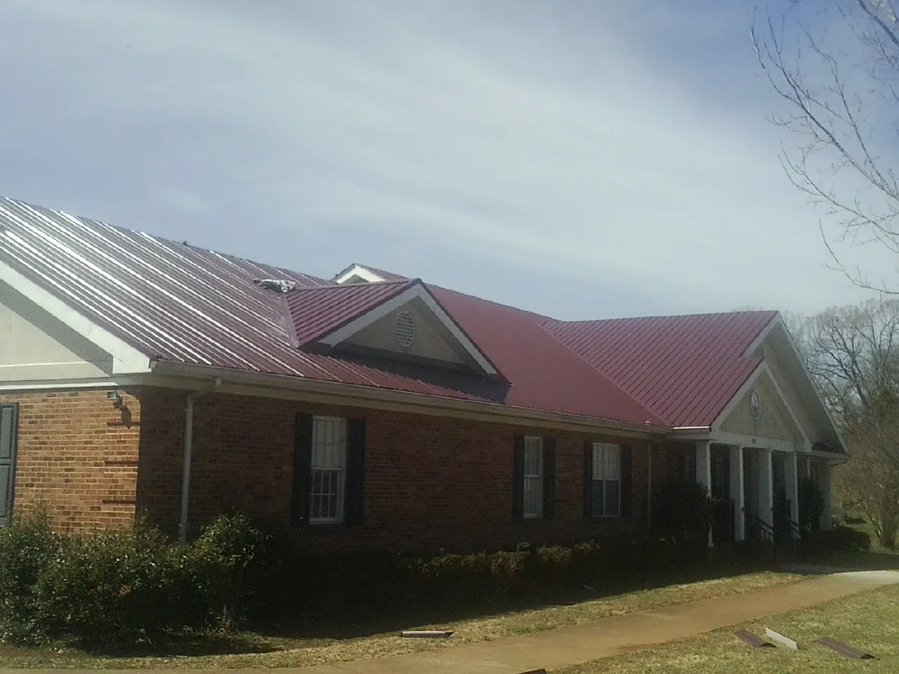 Red metal roof with gabled entries on a long brick building, from a Hail Damage Roof Repair job in Arch Cape