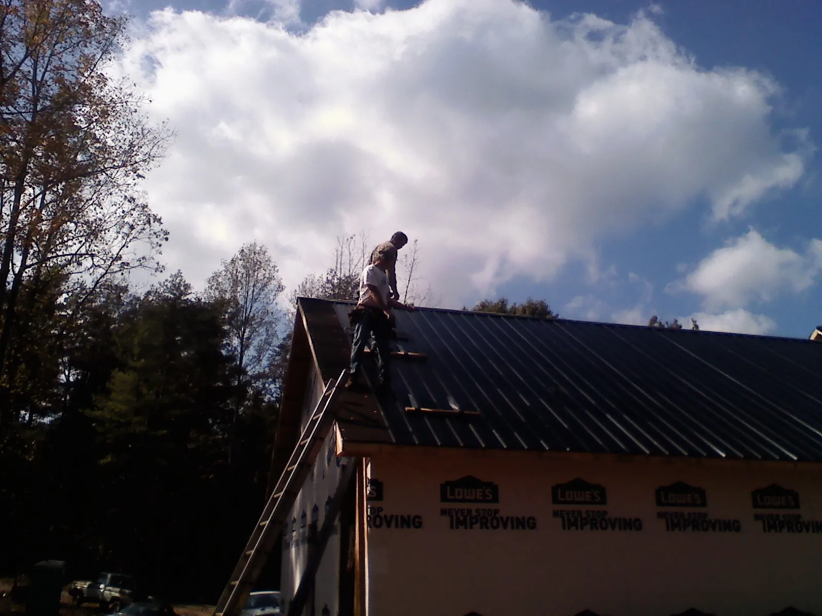 Roofer fastening dark metal panels high against a cloudy sky, from a Roof Inspection job in Arch Cape