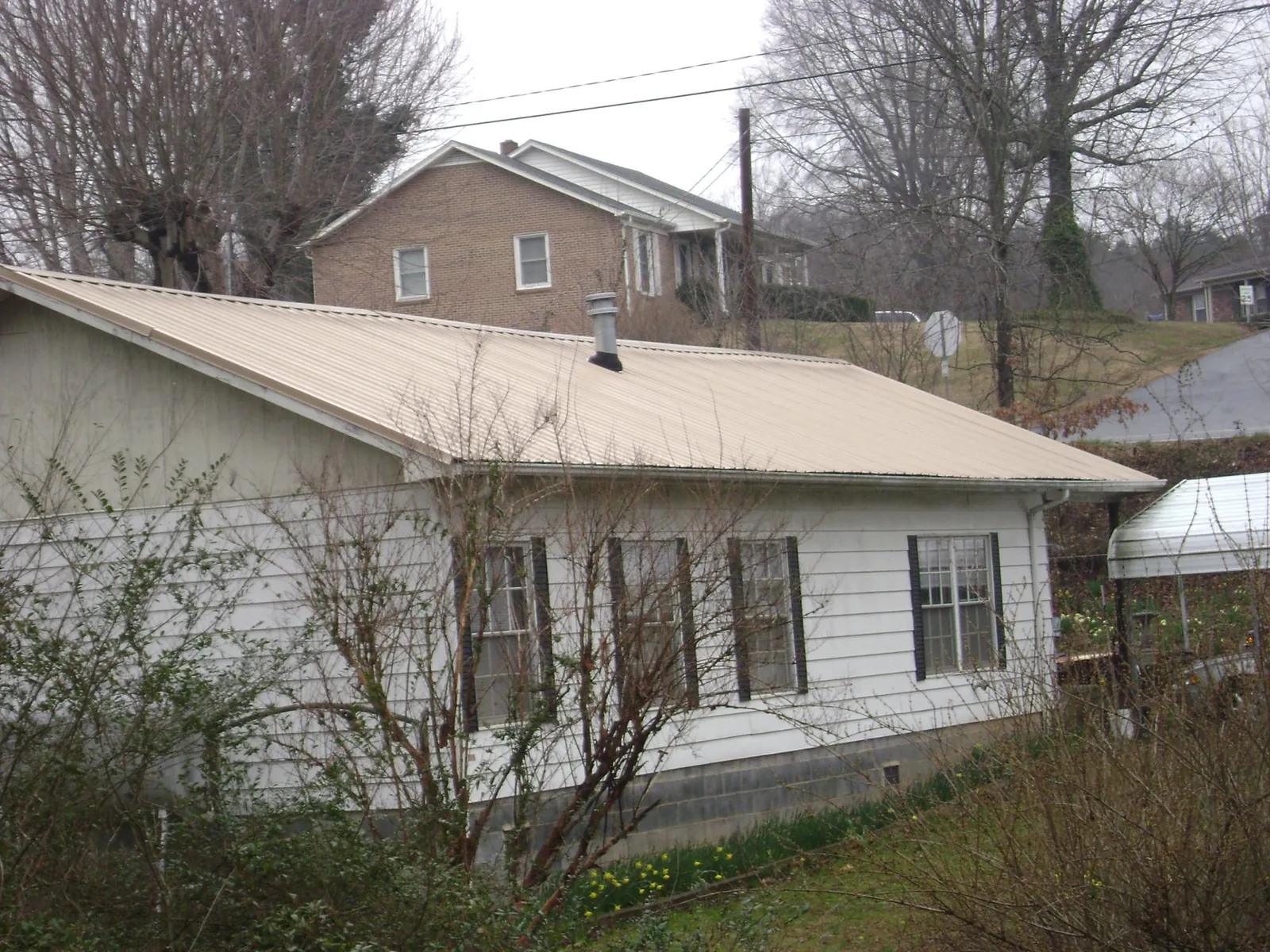Tan metal roof on a white sided house set into a hillside — Commercial Roofing by Roofing Brothers in Arch Cape